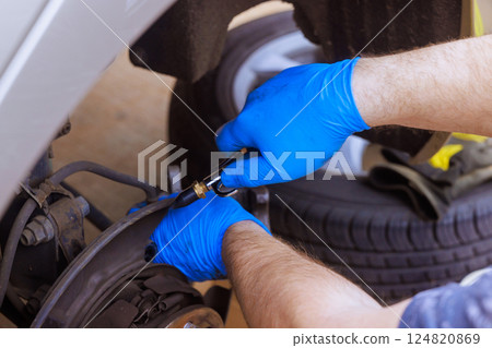 Mechanic wearing gloves inspects repairs brakes on car in well lit garage space during brake assembly 124820869