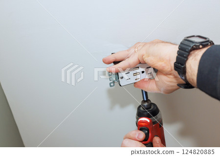 Worker hands secure an electrical outlet to ceiling using cordless drill in home improvement activity. Worker hands secure an electrical outlet to ceiling using cordless drill in home improvement activity. 124820885