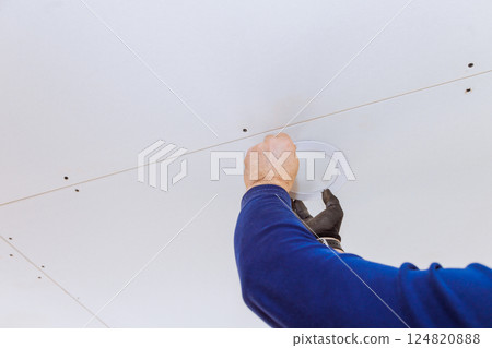 Contractor is placing lighting fixture into ceiling of modern interior space under construction. Contractor is placing lighting fixture into ceiling of modern interior space under construction. 124820888