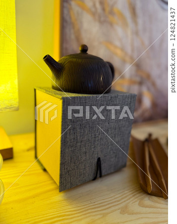 Dark clay teapot resting on textile box under warm light. Calm ritual, mindful aesthetics and cultural appreciation in tea ceremony Dark clay teapot resting on textile box under warm light. Calm ritual, mindful aesthetics and cultural appreciation in tea ceremony 124821437