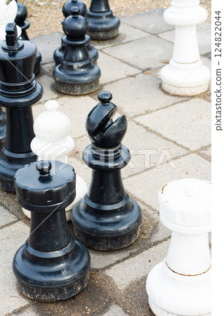 Chess pieces engaging in an intense outdoor match on a sunny day, showcasing the strategic battle between black and white players in a park setting 124822044