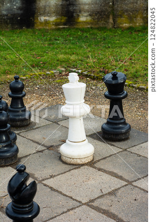 Chess pieces in an outdoor park setting with a solitary white king amidst black pieces on a stone chessboard during a calm afternoon Chess pieces in an outdoor park setting with a solitary white king amidst black pieces on a stone chessboard during a calm afternoon 124822045