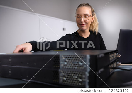 Female IT consultant in datacenter configuring switches in server and network room 124823502