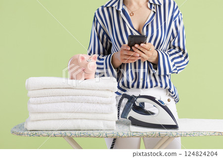Woman holding smartphone next to piggy bank and clean towels Woman holding smartphone next to piggy bank and clean towels 124824204