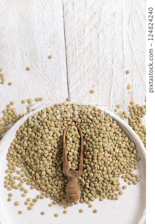 Plate full of dried raw green lentils with a wooden scoop on white table top view. Vegetarian food 124824240