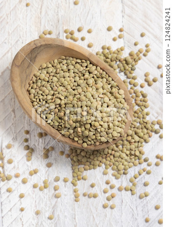 Wooden bowl full of dried green lentils on white table top view. Traditional mediterranean legume Wooden bowl full of dried green lentils on white table top view. Traditional mediterranean legume 124824241