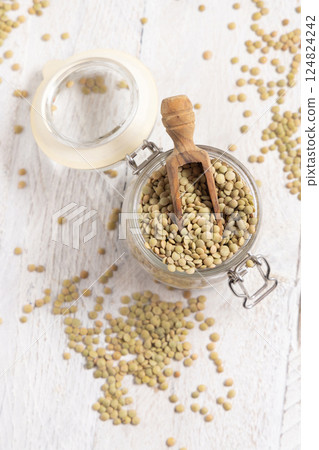 Glass jar full of raw green lentils with a wooden scoop on white table top view. Dried legumes Glass jar full of raw green lentils with a wooden scoop on white table top view. Dried legumes 124824242