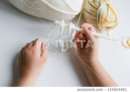 Childs hands crocheting with white and multicolored yarn 124824461
