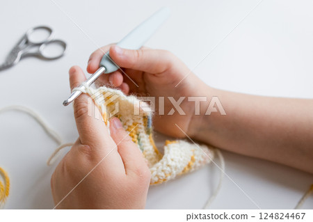 Close up of young caucasian child crocheting with yellow and white yarn 124824467