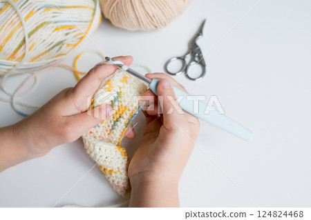 Child crocheting colorful yarn with hook and scissors on table Child crocheting colorful yarn with hook and scissors on table 124824468