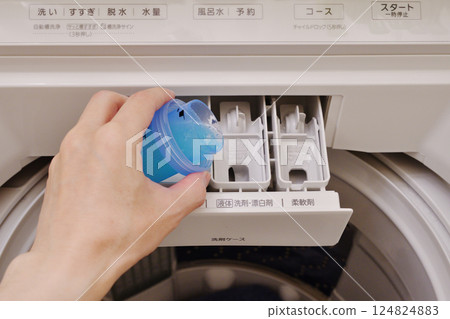 Hands pouring liquid detergent into the detergent compartment of a washing machine 124824883