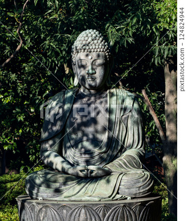 Buddha statue at Senso-ji Temple in Tokyo, Japan, sits in quiet meditation, surrounded lush greenery 124824944
