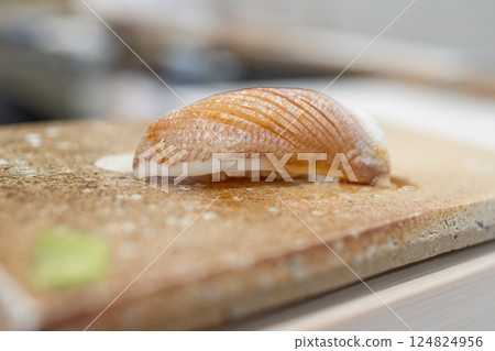 Close-up of a sea bream fry nigiri sushi on a textured cutting board, highlighting delicate texture 124824956