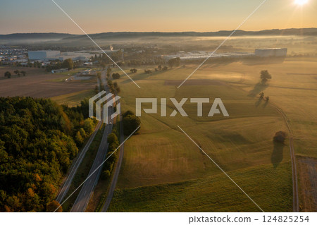 Sunrise scenery, aerial view, with a road passing through nature leading to an industrial area 124825254