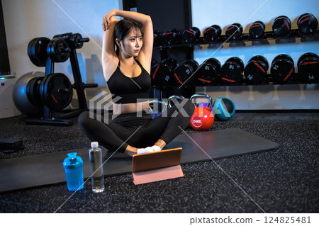 A cool woman stretching at the gym while watching a YouTube video on a tablet How to do it Video viewing 124825481