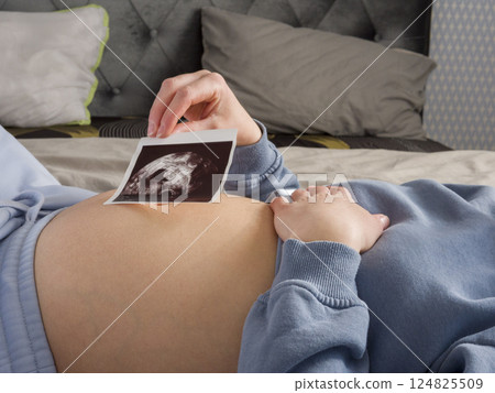 Expectant mother resting peacefully, holding ultrasound image against pregnant belly, experiencing emotional connection with growing baby during prenatal moment 124825509
