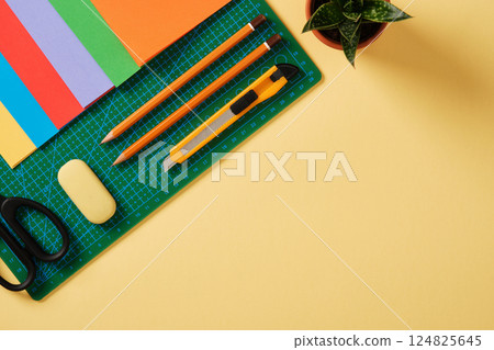 Supplies for paper art hobby: scissors, craft knife, pencil, eraser, colored paper. Space for your text. Paper crafts work table flatlay. 124825645