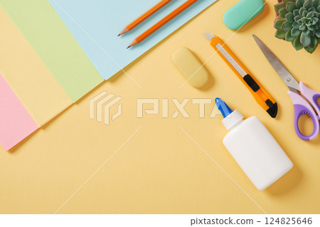 Supplies for paper art hobby in pastel colors: scissors, craft knife, pencil, eraser, colored paper. Space for your text. Paper crafts work table flatlay. 124825646