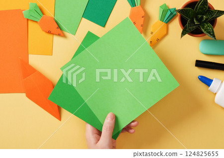 Making a simple origami carrot Easter craft. Take green colored paper to make the haulm. Around the paper creativity tools. 124825655