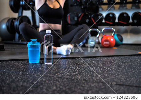 Cool woman stretching at the gym, faceless image, plastic bottle of water, protein shaker Cool woman stretching at the gym, faceless image, plastic bottle of water, protein shaker 124825696