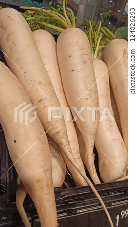 Fresh white daikons with green tops arranged in a black crate at the market. Concept of clean eating, root vegetables and seasonal organic produce Fresh white daikons with green tops arranged in a black crate at the market. Concept of clean eating, root vegetables and seasonal organic produce 124826293