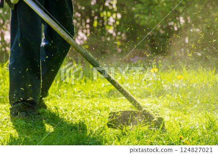 grass cutting in the park with trimmer. sunny outdoor background. lawn care nature concept. scene with working gasoline brushcutter grass cutting in the park with trimmer. sunny outdoor background. lawn care nature concept. scene with working gasoline brushcutter 124827021