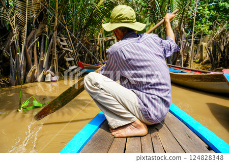 A Vietnamese man paddles a wooden canoe through a rainforest jungle waterway in the Mekong Delta 124828348