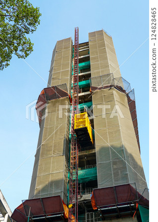 Renovation of a multistory skyscraper, the building is surrounded by scaffolding and a safety net Renovation of a multistory skyscraper, the building is surrounded by scaffolding and a safety net 124828465