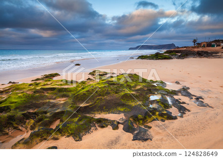 Coastal landscape featuring sandy shores, green seaweed-covered rocks 124828649