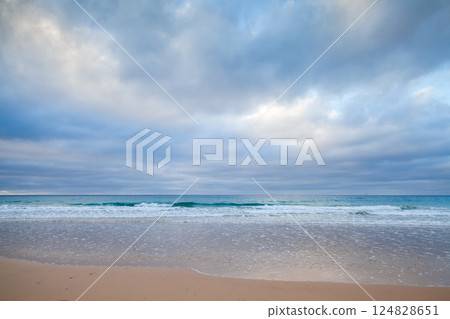 A serene beach view featuring calm waves gently lapping a sandy shore 124828651