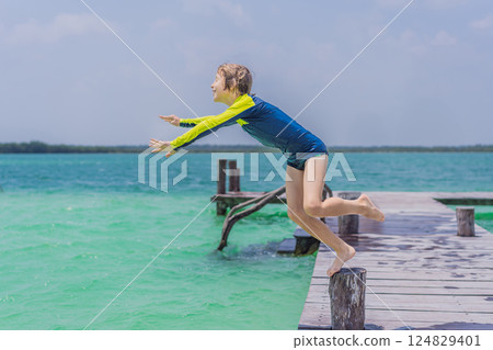 Boy jumping off a pier into a stunning turquoise lagoon in Quintana Roo, Mexico. Joyful summer adventure and tropical travel concept Boy jumping off a pier into a stunning turquoise lagoon in Quintana Roo, Mexico. Joyful summer adventure and tropical travel concept 124829401