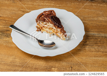 Delicious slice of dessert on a white plate with spoon on wooden table 124829565