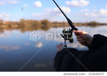 Man catching fish, pulling rod while fishing from lake or pond. Fisherman with rod, spinning reel on river bank. Fishing for pike, perch, carp on beach lake or pond. Wild nature, rural getaway Man catching fish, pulling rod while fishing from lake or pond. Fisherman with rod, spinning reel on river bank. Fishing for pike, perch, carp on beach lake or pond. Wild nature, rural getaway 124830257