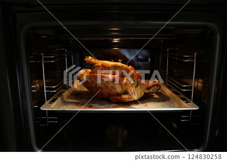 Festive christmas roast whole duck on aluminized steel baking sheet inside open oven at home kitchen. Ready golden turkey or goose on tray. Classic American Thanksgiving food preparation. 124830258