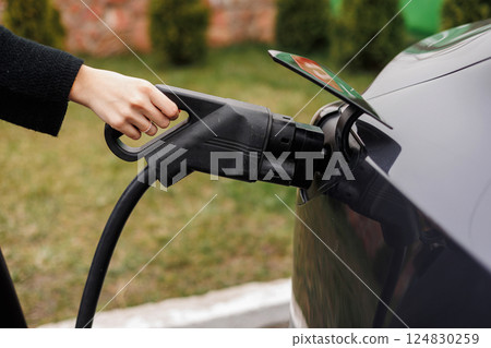 Unrecognisable woman inserting EV charger plug from public or home charging station for modern electric or hybrid car at special place for e-car. Concept eco-friendly sustainability energy car 124830259