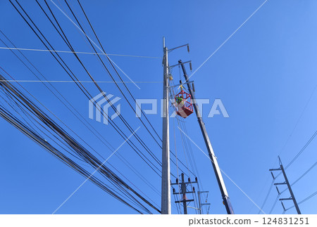 Men in work clothes and hard hats are installing high-voltage wires on a power pole 124831251