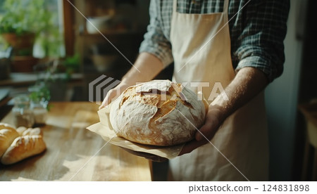 Close-Up Shot Of A Man Holding A Loaf Of Fresh Bread On A Wooden Table Inside A House, Captured Indoors. Close-Up Shot Of A Man Holding A Loaf Of Fresh Bread On A Wooden Table Inside A House, Captured Indoors. 124831898