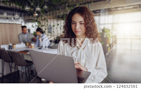 A Young Professional Engaged in Work on a Laptop within a Contemporary Office Environment A Young Professional Engaged in Work on a Laptop within a Contemporary Office Environment 124832501