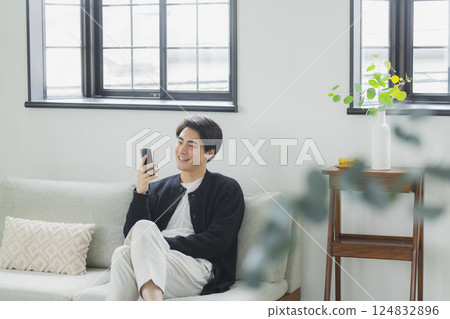 A man who uses a smartphone in the living room A man who uses a smartphone in the living room 124832896