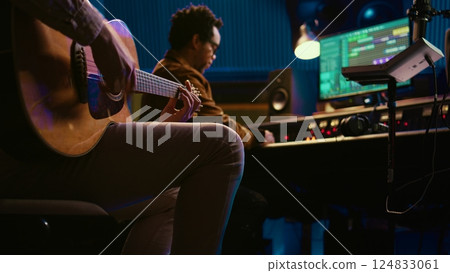 Creative musician singing guitar in professional studio control room, recording his tracks with producer. Singer songwriter composing a new song for his album, editing tunes on console. Camera B. 124833061