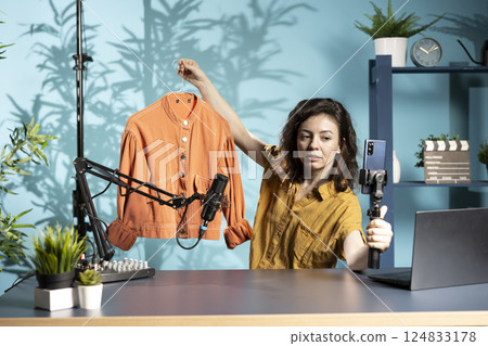 Woman filming fashion vlog, holding jacket in hand, showing subscribers purchases she recently got. Internet show host presenting viewers new clothing acquisition, doing promotion Woman filming fashion vlog, holding jacket in hand, showing subscribers purchases she recently got. Internet show host presenting viewers new clothing acquisition, doing promotion 124833178