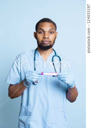 Portrait of doctor holding pregnancy test and doing instructional video for women planning on having kids, blue background. Healthcare staff doing tutorial on how to read pregnancy kit result. 124833197