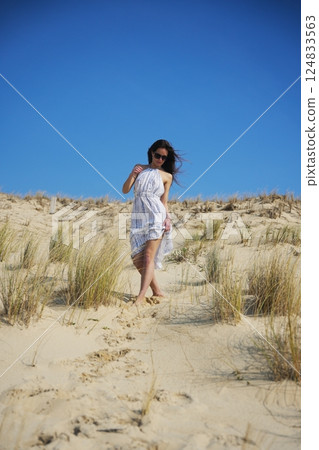 Woman walking barefoot on sandy dune under cloudless summer sky 124833563