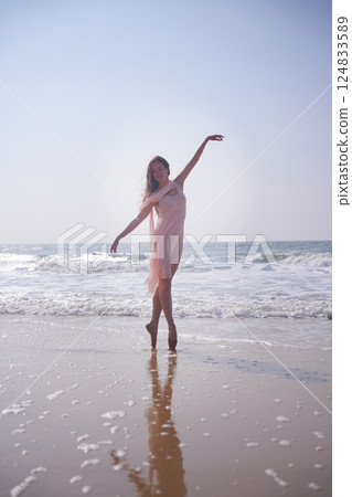 Ballet dancer on pointe in pink dress reflecting in wet sand by the ocean shore 124833589