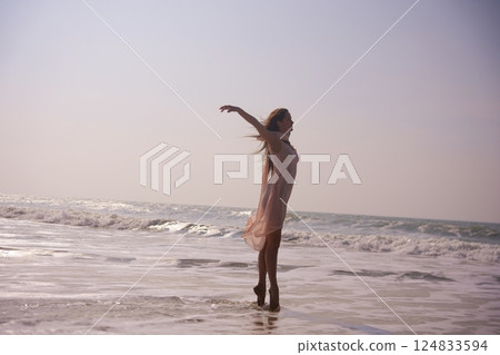 Ballet dancer on seaside en pointe with arms wide open and flowing pink dress 124833594
