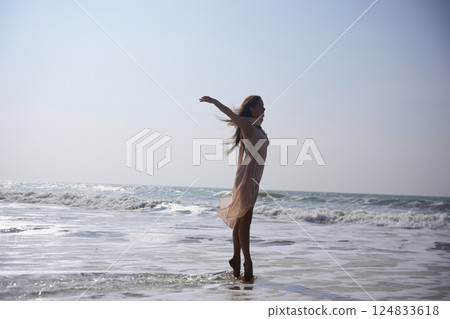 Ballet dancer on toes at ocean shore with arms outstretched and wind her dress Ballet dancer on toes at ocean shore with arms outstretched and wind her dress 124833618