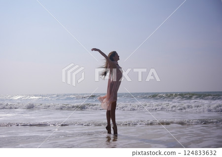 Ballerina on pointe at the ocean edge with arms raised and flowing dress Ballerina on pointe at the ocean edge with arms raised and flowing dress 124833632