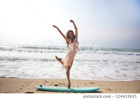 Dreamlike image of ballerina dancing en pointe on surfboard at tranquil seaside 124833635
