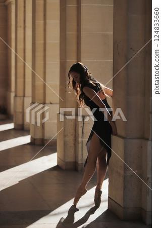 Ballet dancer en pointe leaning gently on column in sunlit stone corridor Ballet dancer en pointe leaning gently on column in sunlit stone corridor 124833660