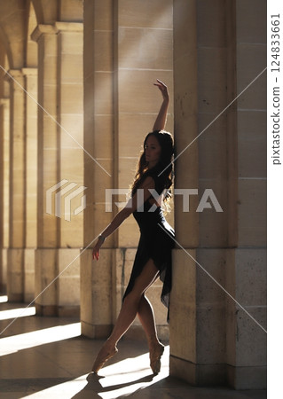Ballet dancer en pointe by stone column in warm classical sunlit corridor 124833661